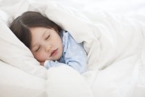 Preschooler girl sleeping under duvet in bed. — Stock Photo