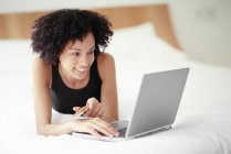 Femme couchée sur le devant du lit et utilisant un ordinateur portable . — Photo de stock