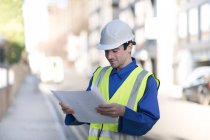 Trabajador de la construcción en sombrero duro y chaqueta de alta visibilidad leyendo plano . - foto de stock