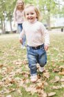 Маленькая девочка бегает в осенних листьях в парке с матерью на заднем плане
. — стоковое фото