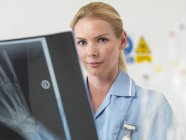 Radióloga femenina mirando en cámara mientras examina imagen de rayos X . - foto de stock