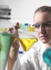 Cientista feminina agitando líquido amarelo em frasco . — Fotografia de Stock