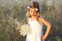Preschooler girl in white dress and floral wreath in field. — Stock Photo