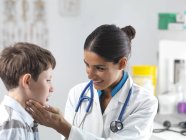 Female pediatrician checking elementary age boy glands. — Stock Photo