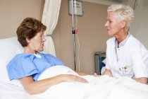 Enfermera y paciente en cama hablando en el hospital . - foto de stock