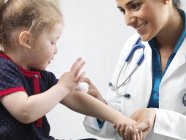 Pediatra femenina limpiando herida en brazo de niña preescolar . - foto de stock