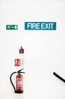 Fire extinguisher, fire alarm and fire exit signs on white wall. — Stock Photo