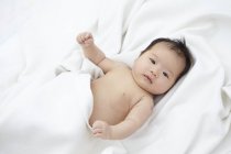 Bambina sdraiata su lenzuola bianche, ritratto . — Foto stock