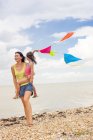 Mother carrying daughter holding bunting on beach. — Stock Photo