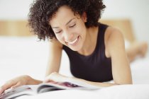 Середня доросла змішана раса жінка читає журнал на ліжку . — стокове фото