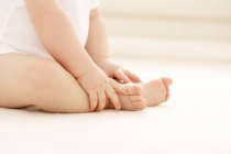 Bebê segurando os pés enquanto sentado no chão . — Fotografia de Stock