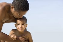 Father holding son against blue sky on beach. — Stock Photo
