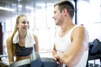 Jeune homme parlant à la femme à la machine d'exercice dans la salle de gym . — Photo de stock