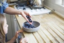 Girl looking as mother pouring fresh blueberries in bowl. — Stock Photo