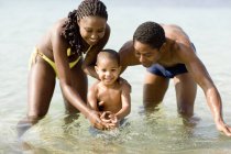 Famille avec enfant d'âge préscolaire jouant dans l'eau de mer . — Photo de stock
