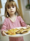 Petite fille préscolaire tenant une assiette de biscuits faits maison et de tartes à la confiture . — Photo de stock