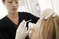 Clinicien examinant le front d'une patiente en tenant la seringue avec injection de botox . — Photo de stock