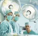 Cirujanos en máscaras quirúrgicas mirando en cámara en quirófano . - foto de stock