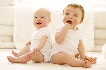 Baby siblings sitting back to back on floor. — Stock Photo