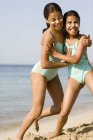 Sisters with sun cream on faces play fighting on beach. — Stock Photo