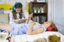 Deux sœurs dans la chambre à coucher écoutant de la musique et utilisant une tablette numérique . — Photo de stock