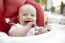 Baby girl eating from spoon in high chair. — Stock Photo