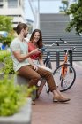 Coppia seduta sulla parete stradale con bici e utilizzando smartphone . — Foto stock