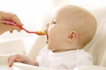 Bambino ragazza mangiare da cucchiaio in seggiolone . — Foto stock