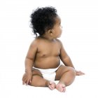 Baby Mädchen sitzt und sieht weg auf weißem Hintergrund. — Stockfoto
