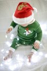 Baby boy in Christmas pajamas playing with fairy lights. — Stock Photo