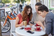 Friends sitting in cafe and using smartphone. — Stock Photo