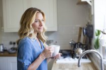 Woman in kitchen with hot drink. — Stock Photo