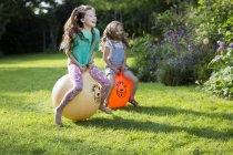 Two sisters bouncing on bouncy hoppers in garden. — Stock Photo
