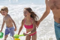 Niños jugando en la playa con balde y pala con los padres . - foto de stock