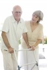 Mujer mayor ayudando a hombre mayor con marco de caminar . - foto de stock