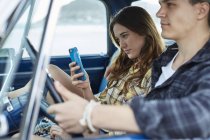 Junges Paar sitzt im Auto, Frau nutzt Smartphone. — Stockfoto