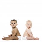Bebê menina e bebê menino sentado de volta para trás no fundo branco . — Fotografia de Stock
