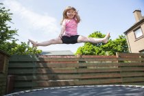 Ragazza in età elementare che salta sul trampolino in giardino . — Foto stock