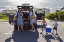 Familie mit zwei Kindern packt Auto aus und trägt Picknickkorb. — Stockfoto