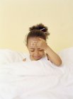 Mädchen im Grundalter hält Kopf mit Fieber im Bett. — Stockfoto