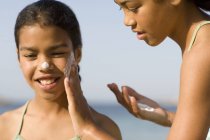Menina aplicando protetor solar ao rosto irmã . — Fotografia de Stock