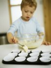 Preschooler boy placing cake mix into paper cases. — Stock Photo