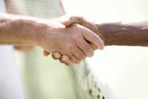 Close-up of two men shaking hands over tennis net. — Stock Photo