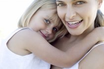 Mother and daughter cuddling and looking in camera outdoors. — Stock Photo
