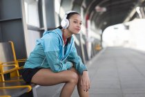 Жінка сидить на залізничні платформи в навушниках — стокове фото