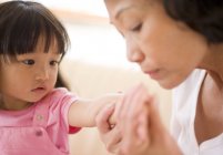 Asiatique grand-mère vérifier pour les signes d'éruption cutanée sur petit-fille bras . — Photo de stock