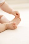 Bebê agarrando grande dedo do pé enquanto sentado no chão
. — Fotografia de Stock