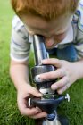 Ginger boy using light microscope on green grass. — Stock Photo