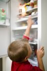 Хлопчик дивиться в холодильник і захоплює їжу . — стокове фото