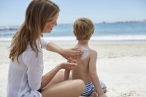 Мати наносить сонячний крем синові на пляжі . — стокове фото